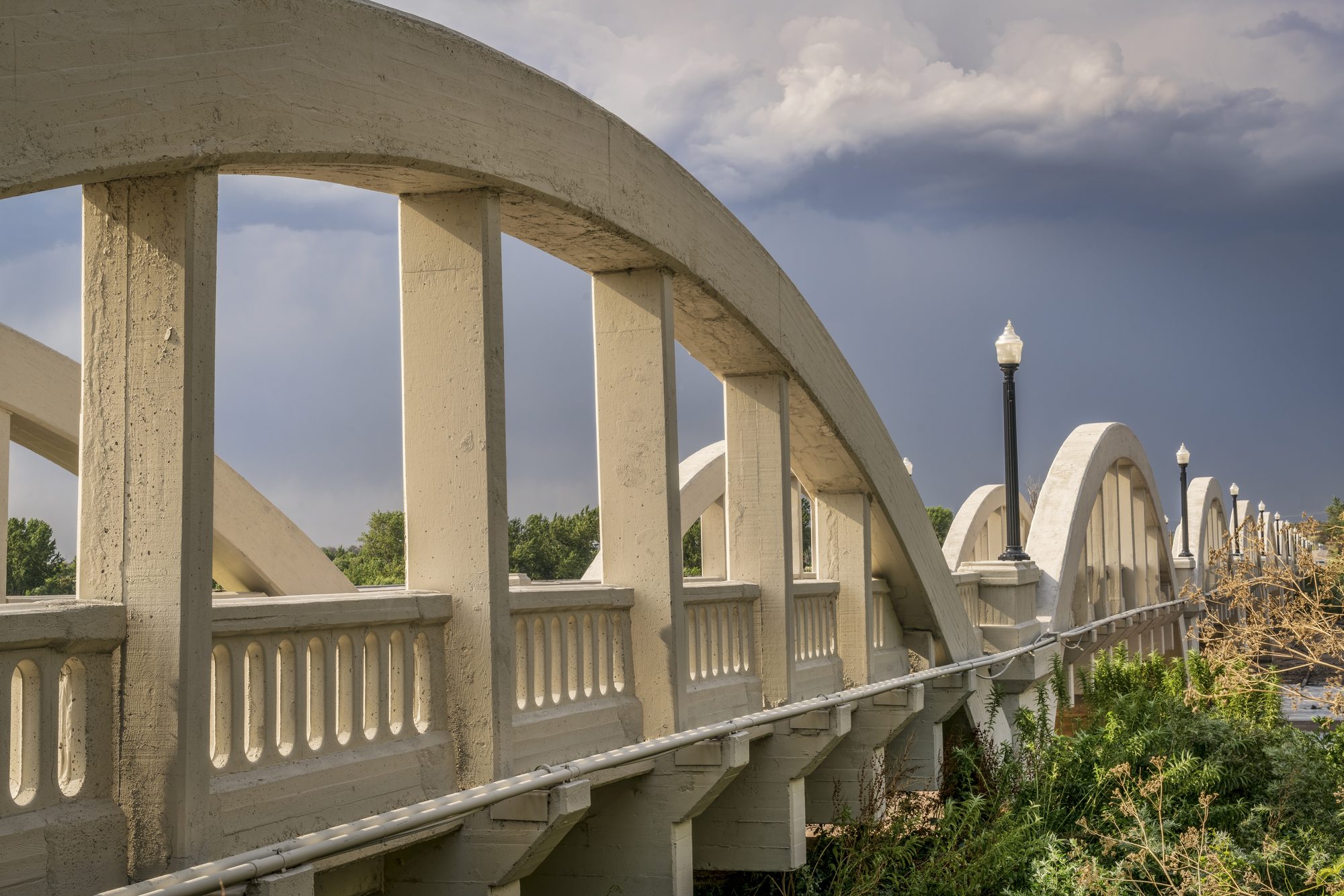 The historic Rainbow Arch Bridge in Fort Morgan, Colorado, against a dramatic prairie sky.